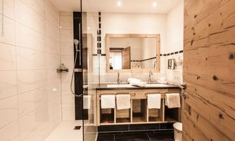 A modern bathroom with a spacious shower and a double-door sink. The walls are in light tones, while the furniture made of wood feels warm.