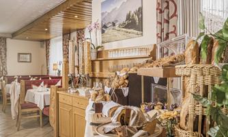 A cozy room with a rich breakfast buffet. On the table, different breads and rolls are arranged in baskets.