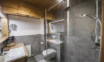 A modern bathroom with a glass shower and elegant wood details. The walls are in neutral gray tones.
