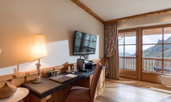 A cozy room with a desk and a television. Large windows offer a view of the mountains.