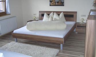 A modern bedroom with a large bed and white pillows. The walls are light, and a piece of art hangs above the bed.