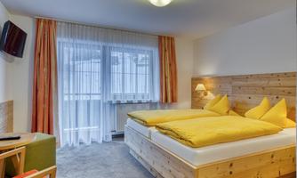 A cozy room with a double bed and yellow cushions. The window provides plenty of daylight and the wood paneling creates a warm atmosphere.