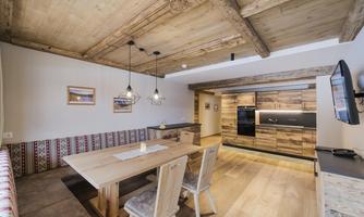 A modern kitchen with wood paneling and a large dining table. The space is bright and cozy.