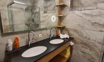 A modern bathroom with two sinks and a wooden shelf. Large mirrors and stylish lighting create an inviting atmosphere.