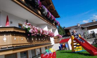 A beautiful house with a flowering balcony and a play area in the garden. A child is playing on the slide in the sunshine.