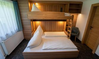 A cozy room with a bunk bed and a double bed. Wooden paneling creates a warm atmosphere.
