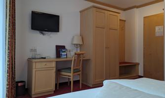 A simple hotel room with a desk, a chair, and a wardrobe. A television is hanging on the wall.