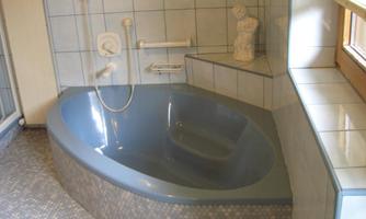 A modern bathroom with an elegant, blue oval-shaped bathtub. The walls are tiled, and a statue decoratively stands in the room.
