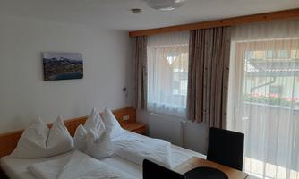 A bright hotel room with two beds and a table. Large windows provide plenty of daylight.