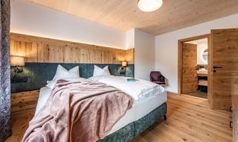 A modern bedroom with a large bed and a cozy blanket. Wooden elements and warm light create an inviting atmosphere.
