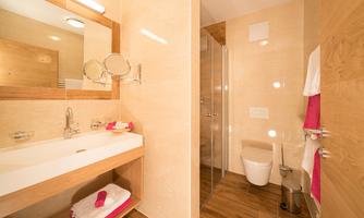 A modern bathroom with wood and tile elements. It features a sink, a large mirror, and a shower.