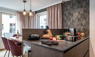 A modern kitchen with a kitchen island and elegant pendant lights. Fresh ingredients are on the countertop, while the dining area with red chairs looks inviting.