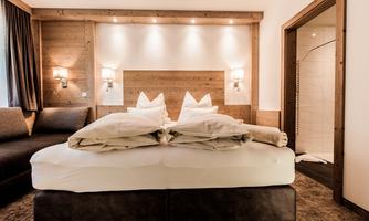 A modern hotel room with a large double bed and two cozy pillows. The wooden walls and soft lighting create a warm atmosphere.