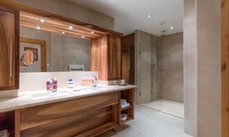 A modern bathroom with a wooden vanity and large mirror surfaces. The shower is open and stylishly designed, featuring neutral colors and bright lighting.