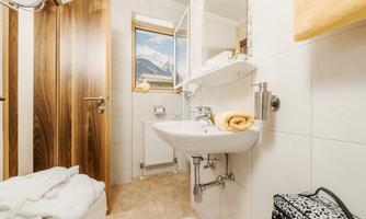 A modern bathroom with a sink and a large mirror. Through the window, you can see mountains, and the surroundings are bright and inviting.