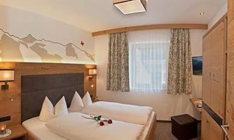 A cozy bedroom with a double bed, wooden-paneled walls, and soft lighting. The windows are decorated with curtains.