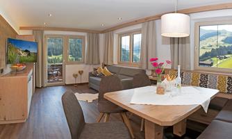 A cozy holiday apartment with modern furnishings. Large table, sofa, and a view of the surrounding mountains through large windows.