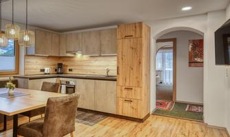 A modern kitchen with wooden cabinets and a dining table. The room is bright and inviting, with access to another room in the background.