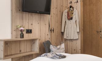 A cozy room with wooden paneling and a television on the wall. A coat hangs on a hook, and a flower vase sits on a shelf.
