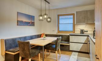 A modern kitchen with a dining table and cozy seating. Large windows provide plenty of daylight.