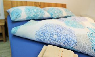 A cozy bed with colorful pillows and a decorative quilt. Fresh towels are beside the bed.