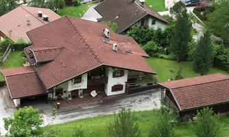 A pretty house with a red roof, surrounded by lush greenery and trees. The property is well-maintained and has an inviting garden.