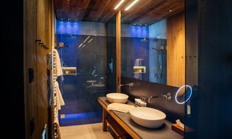 A modern bathroom featuring wood and glass elements. It includes two sinks and stylish lighting.