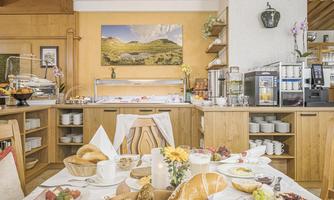 A cozy restaurant with a hearty breakfast buffet. The table is set with various rolls, fruits, and drinks.