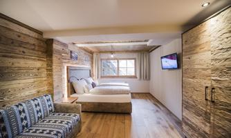 A modern bedroom with two beds and a comfortable sofa. Wood paneling and large windows create a cozy atmosphere.