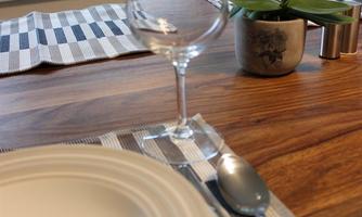 A set table with a white plate, cutlery, and a wine glass. In the background, there are windows overlooking green trees and a small orchid on the table.
