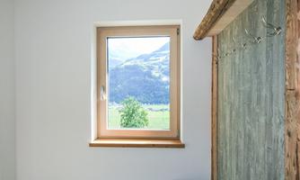 A bright room with a window that overlooks a green landscape and mountains. On the wall, there is a wooden structure with hooks.