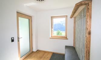 A bright entrance area with a glass door and a window. There is a wooden bench and a natural wall.