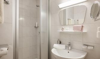 A modern bathroom with a shower and a sink. The walls are brightly tiled and there are practical shelves.