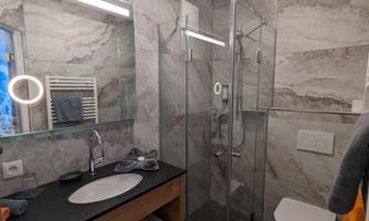 A modern bathroom with a glass shower and a simple sink. The walls are clad with elegant marble slabs.