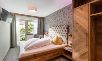 A modern bedroom with a cozy bed and wooden furniture. The room has large windows and a decorative wall.