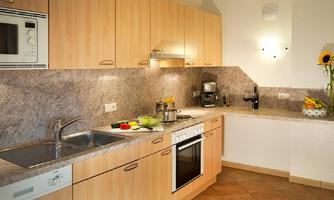 A modern kitchen with wooden cabinets and a bright countertop. Fresh vegetables and kitchen appliances are visible on the countertop.