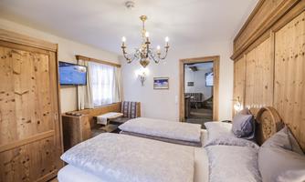 A cozy room with two beds and wooden paneling. There is a television and a beautifully decorated chandelier.