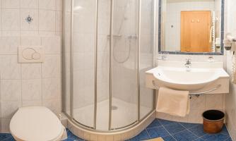 A small bathroom with a shower and a sink. The walls are tiled and the floor is blue with a light carpet.
