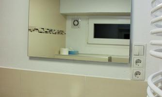 A modern bathroom with a bright sink and a large mirror. In the background, windows and a heater can be seen.