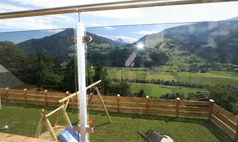 A beautiful view from a balcony of a green landscape with mountains in the background. The area is equipped with a wooden railing and playground equipment.