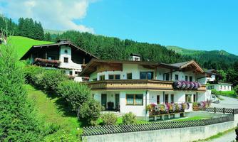 A picturesque Alpine landscape with traditional chalets and blooming flowers. In the background are green hills and a clear blue sky.
