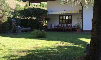 A cozy house with a large garden. The terrace is equipped with wooden chairs and a sun umbrella.