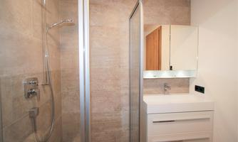 The image shows a modern bathroom with a shower and a sink. The walls are painted in neutral tones, which conveys a clean and elegant impression.
