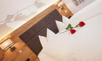 A cozy bedroom with a large bed and elegant decoration. Two red roses lie on the bedspread, creating a romantic atmosphere.