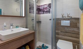 A modern bathroom with a shower and a sink. The walls are tiled in light colors and adorned with decorative elements.