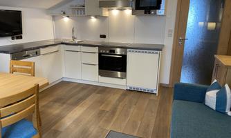 A modern kitchenette with appliances and a wooden floor. A dining table with chairs and a cozy sofa are also visible.