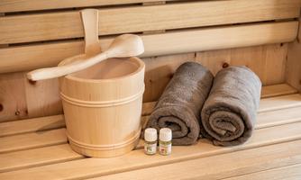 A relaxing sauna setting with a wooden container, a wooden spoon, and two gray towels. There are also two small bottles of essential oils visible.
