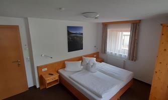 A simple hotel room with a double bed and a small nightstand. The room has a window with daylight and a picture on the wall.