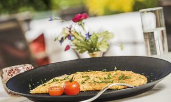A fried salmon on a black plate, garnished with fresh herbs. In the background, a flower and a glass of water are visible.