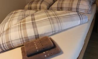 A cozy bedroom with a bed dressed in plaid blankets and pillows. At the foot of the bed lie two towels.